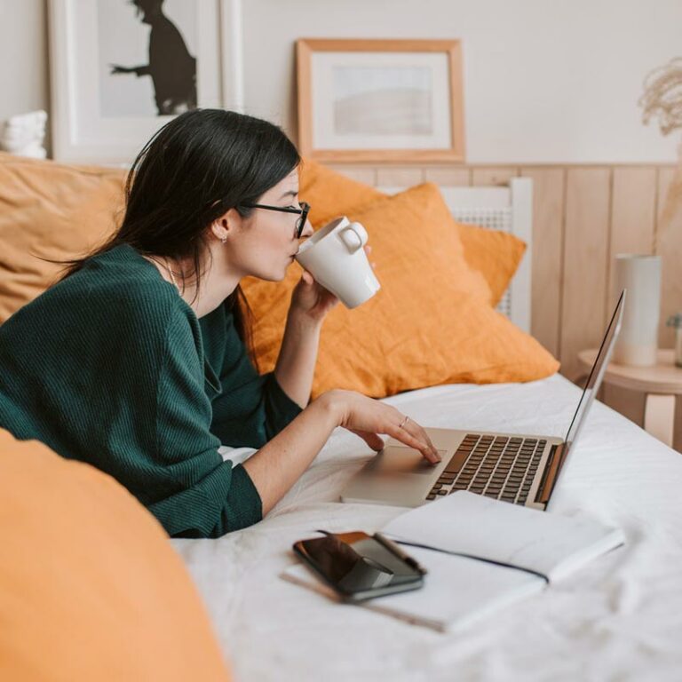Femme couchée sur son lit buvant une tasse thé et suivant un cours d'e-learning de Luno Académie sur son ordinateur